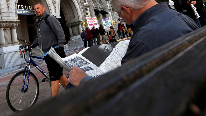 A man reads a newspaper story about Republican U.S. presidential nominee Donald Trump as people gather to protest against Trump on the sidewalk, outside the grand opening of his new Trump International Hotel in Washington, U.S. October 26, 2016. REUTERS/Jonathan Ernst - S1AEUJFELYAA