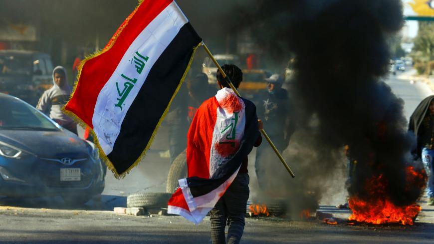 A demonstrator carries an Iraqi flag as he walks near burning tires, during ongoing anti-government protests in Najaf, Iraq January 12, 2020. REUTERS/Alaa al-Marjani - RC2BEE9XMY8P