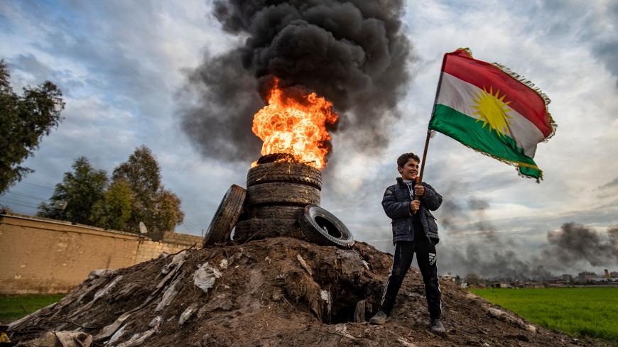 A boy stands holding a Kurdish flag near a bonfire marking the Kurdish holiday of Noruz in Qamishli in Syria's northeastern Hasakah province on March 20, 2020, after the local authorities cancelled holiday celebrations due to fears of the spread of COVID-19 coronavirus disease. - The Persian New Year is an ancient Zoroastrian tradition celebrated by Iranians and Kurds which coincides with the vernal (spring) equinox and is calculated by the solar calendar. (Photo by DELIL SOULEIMAN / AFP) (Photo by DELIL SO