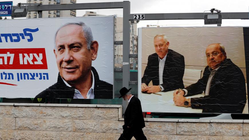 An ultra-Orthodox Jewish man walks next to Likud party election campaign banners, one depicting party leader Israeli Prime Minister Benjamin Netanyahu and the other depicting Benny Gantz, head of Blue and White party and Ahmad Tibi, co-leader of the Joint List, an Arab party, in Jerusalem February 20, 2020. Picture taken February 20, 2020. REUTERS/Ammar Awad - RC297F9OEC8G