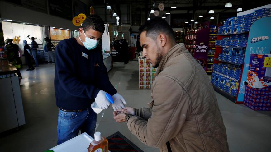 A Palestinian worker wearing a mask sanitizes the hands of a customer amid coronavirus precautions, in a supermarket in Gaza City March 8, 2020. Picture taken March 8, 2020. REUTERS/Mohammed Salem - RC2EGF9PKI3K