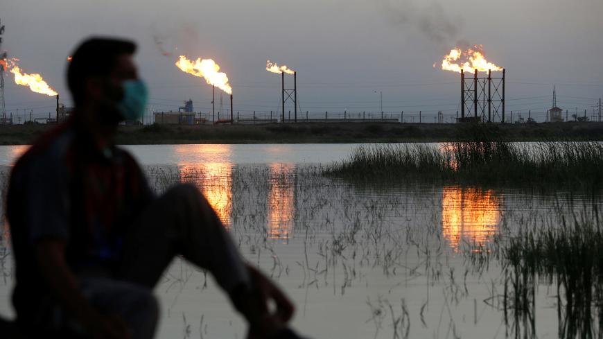 Flames emerge from flare stacks at Nahr Bin Umar oil field, as a man is seen wearing a protective face mask, following the outbreak of the coronavirus, north of Basra, Iraq March 9, 2020. REUTERS/Essam Al-Sudani - RC2IGF9A1IYO
