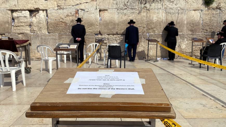 Ultra-Orthodox Jewish men pray in front of the Western Wall, Judaism's holiest prayer site, in Jerusalem's Old City as a note advice not to kiss the stones of the Western Wall display  March 16, 2020 REUTERS/ Ilan Rosenberg - RC21LF90G2FL