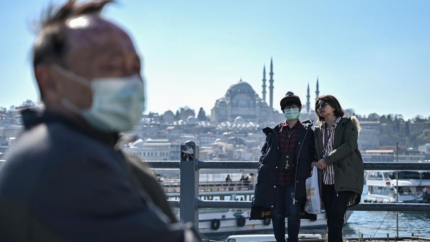 Tourists wearing face masks sit and stand on Galata bridge in Istanbul, on March 13, 2020, amid the outbreak of COVID-19, the new coronavirus. - Turkey said on March 12 it would shut all schools for two weeks and bar spectators from football matches through April after recording its first case of the new coronavirus. The death toll from the coronavirus pandemic has risen to 5,043, according to an AFP tally based on official sources at 1100 GMT on March 13. Since COVID-19 was first detected in December 2019,