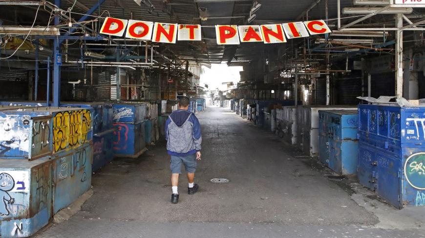 A man passes under a "Don't Panic" banner hanging at the entrance of Shuk HaCarmel (Caramel) market in the Israeli coastal city of Tel Aviv on March 24, 2020 after Israel barred residents from leaving home for non-essential reasons and stopped night-time public transport, tightening already strict measures to fight the spread of coronavirus. (Photo by JACK GUEZ / AFP) (Photo by JACK GUEZ/AFP via Getty Images)