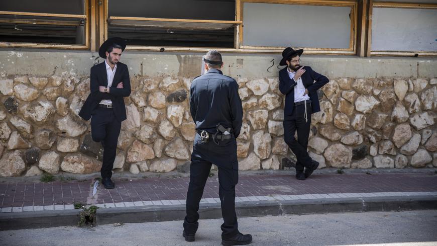 02 April 2020, Israel, Bnei Brak: An Israeli policeman stops Orthodox Jews, who insist on carrying on with their prayer at the Ponevezh Yeshiva, a Jewish institution that focuses on the study of traditional religious texts, despite the imposed lockdown amid the coronavirus pandemic. Photo: Ilia Yefimovich/dpa (Photo by Ilia Yefimovich/picture alliance via Getty Images)