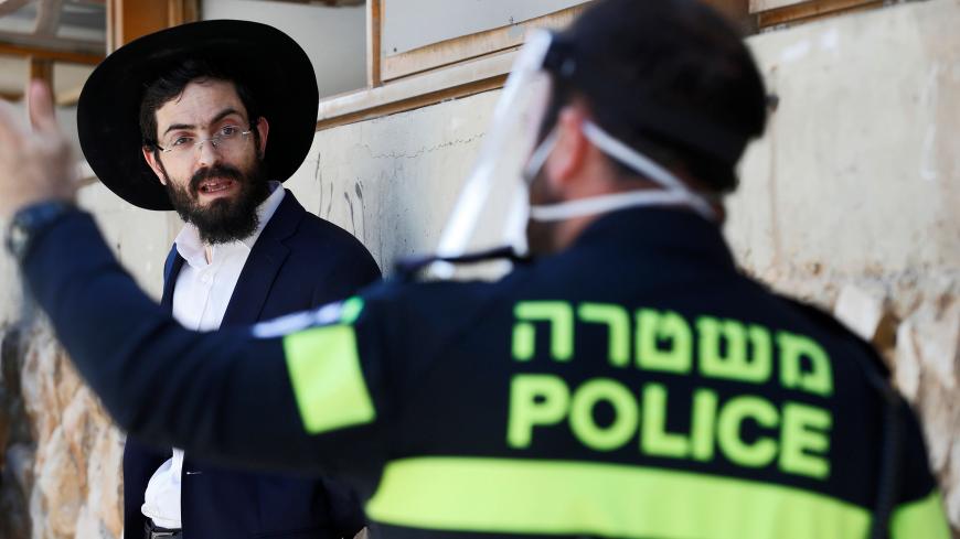 An Israeli police officer speaks to an ultra-Orthodox Jewish student at a Yeshiva (Talmudic school) in Bnei Barak, a city east of Tel Aviv with a significant ultra-Orthodox Jewish population, on April 2, 2020, as part of measures imposed by Israeli authorities against the COVID-19 coronavirus pandemic. - Israeli police backed by surveillance helicopters have stepped up patrols of ultra-Orthodox Jewish neighbourhoods that have become coronavirus hotspots. (Photo by JACK GUEZ / AFP) (Photo by JACK GUEZ/AFP vi