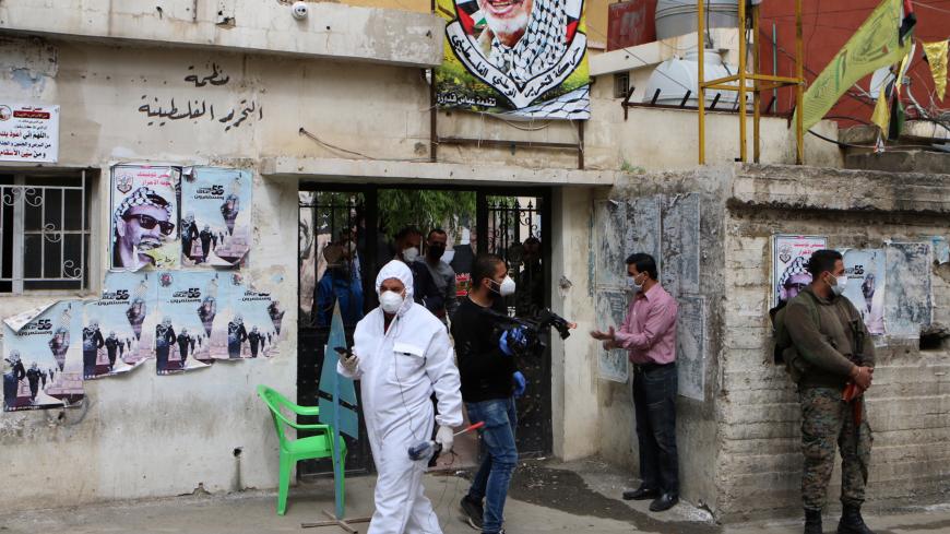 A health worker and armed Palestinians gather under the portrait of their late leader Yasser Arafat at the Wavel Palestinian refugee camp (also known as the Jalil camp) in Lebanon's eastern Bekaa Valley, on April 24, 2020, after cases of infection by the novel coronavirus were detected there. - The residents of the Wavel camp were tested after a member of a household, a Palestinian refugee from Syria, was admitted to the state-run Rafic Hariri hospital in the capital Beirut  for demonstrating COVID-19 sympt