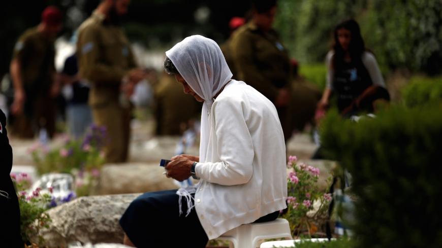 An Israeli woman reads a holy book as she sits next to a grave during the Memorial Day for the Israeli fallen soldiers in the Military cemetery in Mount Herzl in Jerusalem May 1, 2017  REUTERS/Ronen Zvulun - RC11DA2145E0