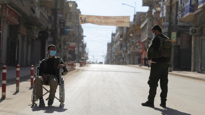 A member of the Asayish stands near a man in a wheelchair along an empty street, as restrictions are imposed as measure to prevent the spread of the coronavirus disease (COVID-19) in Qamishli, Syria March 23, 2020. REUTERS/Rodi Said - RC2VPF9ALD0J