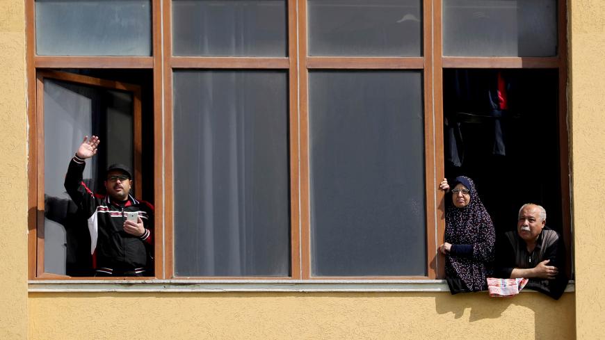 Palestinians, who are quarantined at Al-Mathaf Hotel amid concerns about the spread of the coronavirus disease (COVID-19), wave to their relatives in the northern Gaza Strip April 15, 2020. REUTERS/Mohammed Salem - RC225G9AJ5UK