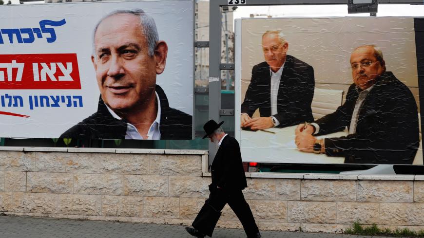 An ultra-Orthodox Jewish man walks next to Likud party election campaign banners, one depicting party leader Israeli Prime Minister Benjamin Netanyahu and the other depicting Benny Gantz, head of Blue and White party and Ahmad Tibi, co-leader of the Joint List, an Arab party, in Jerusalem February 20, 2020. Picture taken February 20, 2020. REUTERS/Ammar Awad - RC297F9OEC8G
