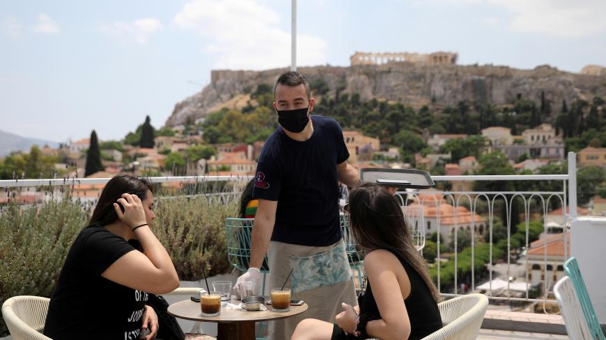 A waiter wearing a protective face mask serves customers in a coffee shop, with the Acropolis hill in the background, as restaurants reopen following the easing of measures against the spread of the coronavirus disease (COVID-19), in Athens, Greece May 25, 2020. REUTERS/Costas Baltas - RC2NVG9ZZ8UZ