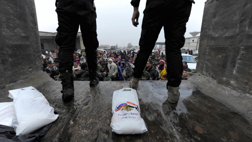 Russian soldiers stand near food aid being distributed to Syrians evacuated from eastern Aleppo, in government controlled Jibreen area in Aleppo, Syria November 30, 2016. The text on the bag, showing Syrian and Russian national flags, reads in Arabic: "Russia is with you".  REUTERS/Omar Sanadiki - RC195E2ECA60