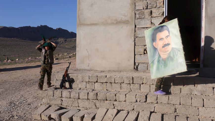 A female Kurdistan Workers Party (PKK) fighter adjusts her scarf while another carries a picture of jailed Kurdish militant leader Abdullah Ocalan at their base in Sinjar March 11, 2015. Women fighters at a PKK base on Mount Sinjar in northwest Iraq, just like their male counterparts, have to be ready for action at any time. Smoke from the front line, marking their battle against Islamic State, which launched an assault on northern Iraq last summer, is visible from the base. Many of the women have cut links