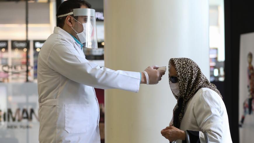 A man wears a face mask and a protective face shield as he checks a woman's temperature, to let her go inside the mall, following the outbreak of the coronavirus disease (COVID-19), after shopping malls and bazaars reopened in Tehran, Iran, April 20, 2020. WANA (West Asia News Agency)/Ali Khara via REUTERS ATTENTION EDITORS - THIS PICTURE WAS PROVIDED BY A THIRD PARTY? - RC2F8G9RTNFI