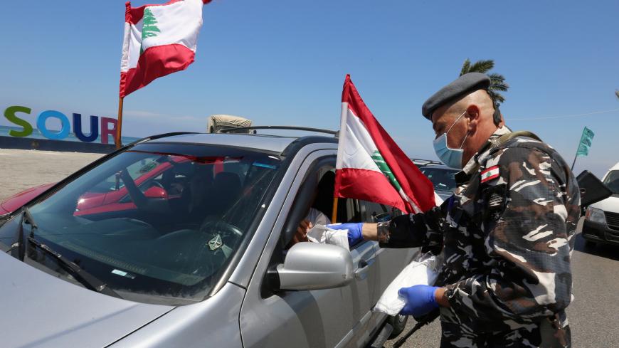 A member of internal security forces distributes protective masks for demonstrators, as preventive measures against the spread of coronavirus disease (COVID-19), during a protest in cars against the growing economic hardship and to mark Labour Day in Tyre, Lebanon May 1, 2020. REUTERS/Aziz Taher - RC2OFG96BP4S
