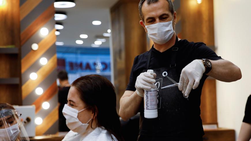Hairdresser Oguz Kutlu disinfects scissors as he gives hair treatment to his customer Pinar Ersin, both wearing protective masks, on the first day of the reopening of his hair salon which was closed since March 21 amid the spread of the coronavirus disease (COVID-19), in Istanbul, Turkey, May 11, 2020. REUTERS/Umit Bektas - RC2BMG9VSKGF