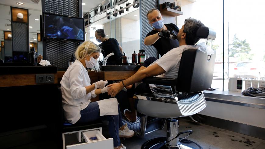 An employee trims beard of a client as the other one gives him manicure, on the first day of the reopening of a hair salon which was closed since March 21 amid the spread of the coronavirus disease (COVID-19), in Istanbul, Turkey, May 11, 2020. REUTERS/Umit Bektas - RC2BMG9ZPB5E
