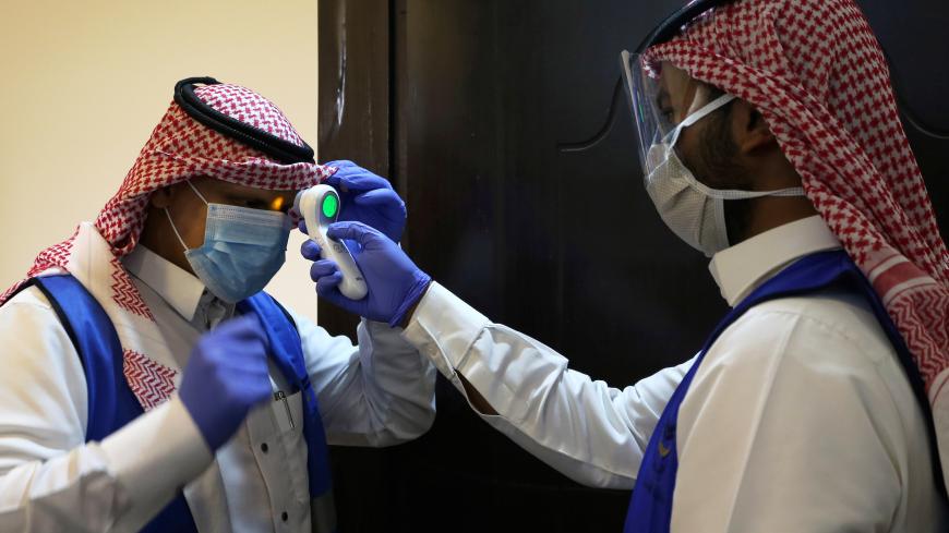 A Saudi volunteer supervisor wearing a protective face mask and gloves checks the temperature of another volunteer before preparing boxes of Iftar meals provided by a charity organisation following the outbreak of the coronavirus disease (COVID-19), during the holy month of Ramadan, in Riyadh, Saudi Arabia May 10, 2020. Picture taken May 10, 2020. REUTERS/Ahmed Yosri - RC2WMG9RFHBL