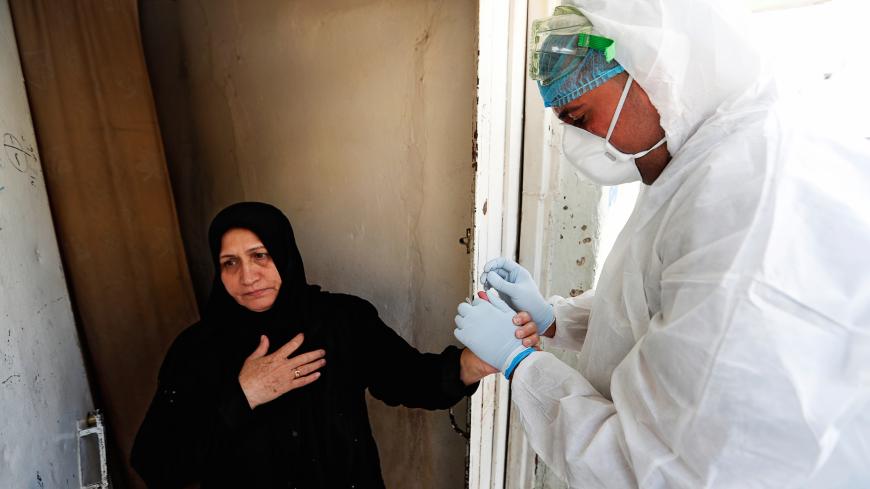A healthcare worker takes blood samples from a woman during testing for the coronavirus disease (COVID-19) in Sadr city, district of Baghdad, Iraq May 21, 2020. REUTERS/Thaier Al-Sudani - RC21TG9DOH2Z