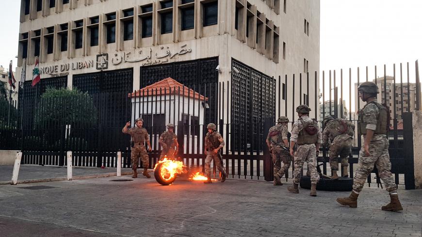 Lebanese Army soldiers roll away a flaming tire from the fence surrounding the local branch of the Banque du Liban (Lebanese Central Bank) as protesters gather to demonstrate against dire economic conditions in the northern city of Tripoli on June 11, 2020. - The Lebanese pound sank to a record low on the black market on June 11 despite the authorities' attempts to halt the plunge of the crisis-hit country's currency, money changers said. Lebanon is in the grips of its worst economic turmoil in decades, and