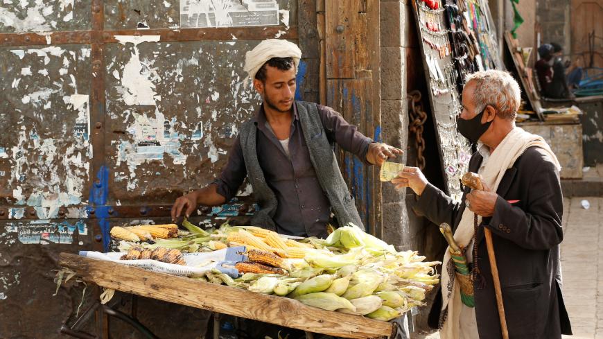 A man wearing a protective mask buys corn from a street vendor at a market amid novel coronavirus spread concerns in the old quarter of Sanaa, Yemen June 2, 2020. REUTERS/Khaled Abdullah - RC241H9PGGBD