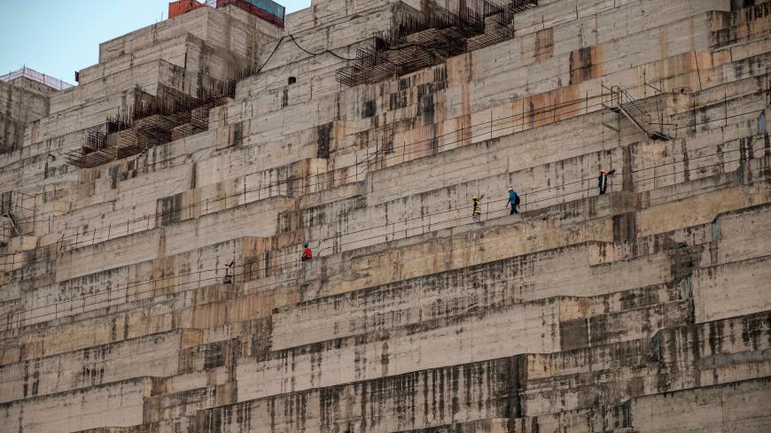 Workers walk along the Grand Ethiopian Renaissance Dam (GERD), near Guba in Ethiopia, on December 26, 2019. - The Grand Ethiopian Renaissance Dam, a 145-metre-high, 1.8-kilometre-long concrete colossus is set to become the largest hydropower plant in Africa.
Across Ethiopia, poor farmers and rich businessmen alike eagerly await the more than 6,000 megawatts of electricity officials say it will ultimately provide. 
Yet as thousands of workers toil day and night to finish the project, Ethiopian negotiators re