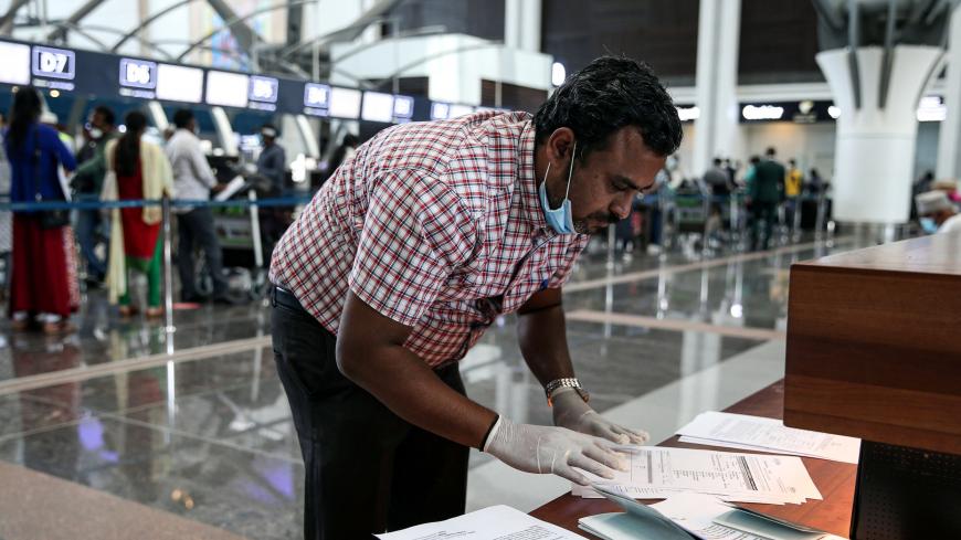 A man wearing latex gloves and a mask, due to the COVID-19 coronavirus pandemic, checks airline tickets and travel documents while behind him Indian nationals residing in Oman queue with their luggage at the check-in counter at a terminal in Muscat International Airport ahead of their repatriation flight from the Omani capital, on May 12, 2020. (Photo by MOHAMMED MAHJOUB / AFP) (Photo by MOHAMMED MAHJOUB/AFP via Getty Images)
