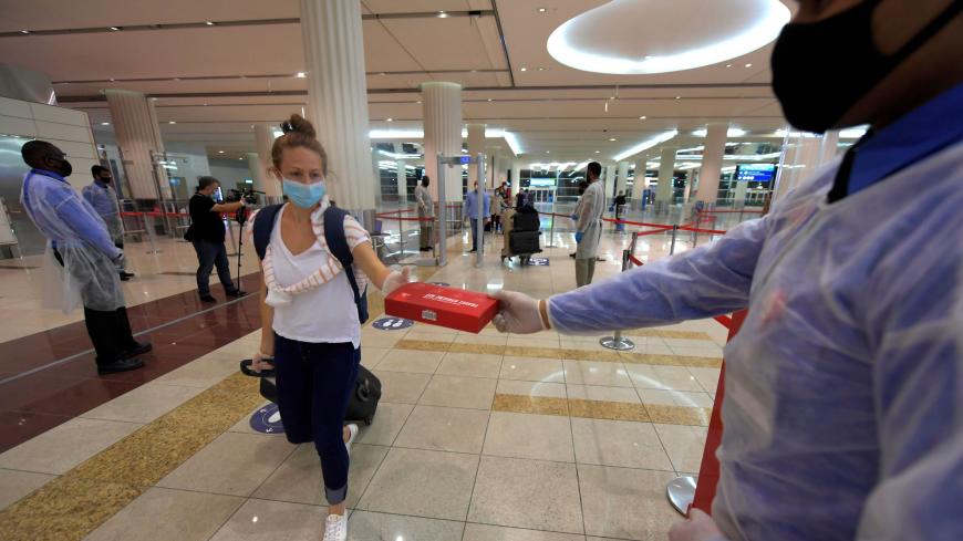 A passengers of an Emirates airlines flight departing to the Australian city of Sydney, receives a box of masks and gloves at Dubai International Airport on May 22, 2020, after the resumption of scheduled operations by the Emirati carrier, amid the ongoing novel coronavirus pandemic crisis. (Photo by Karim SAHIB / AFP) (Photo by KARIM SAHIB/AFP via Getty Images)