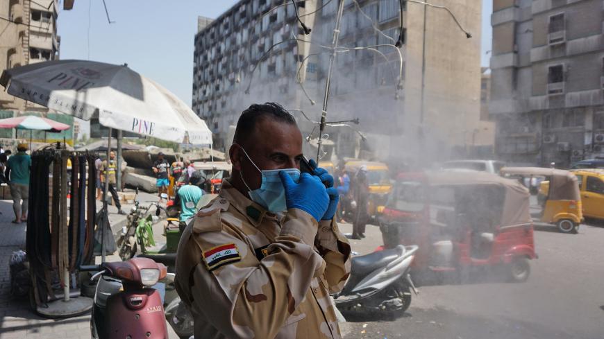 An Iraqi policeman, wearing a protective mask and gloves due to the COVID-19 pandemic, stands by a water sprinkler on a hot summer day in Baghdad on July 7, 2020. (Photo by SABAH ARAR / AFP) (Photo by SABAH ARAR/AFP via Getty Images)