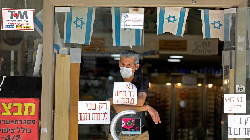 A man wearing a protective mask amid the Covid-19 pandemic stands in a shop with a sign on the window reading in Hebrew: please wear a mask in the centre of Jerusalem on July 7, 2020. - As of today, Israel had recorded more than 31,000 coronavirus cases, including 338 deaths. In recent weeks, the country of about nine million people has regularly registered between 500 to 1,000 new cases each day. (Photo by MENAHEM KAHANA / AFP) (Photo by MENAHEM KAHANA/AFP via Getty Images)
