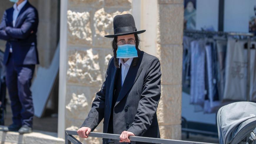 An Ultra-Orthodox Jewish man, wearing a protective face mask, stands at a checkpoint erected to block entrance to the neighbourhoods of Romema and Kiryat Belz after authorities imposed a lockdown to combat the spread of the Coronavirus, in Jerusalem on July 12, 2020. (Photo by AHMAD GHARABLI / AFP) (Photo by AHMAD GHARABLI/AFP via Getty Images)