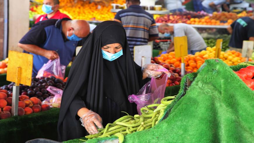 An Iraqi woman wearing a protective mask amid the COVID-19 pandemic, buys fresh produce from a street seller at a market in Karrada, in the capital Baghdad, on July 14, 2020. - Iraq, in a bid to prevent the spread of the deadly COVID-19 illness, shut its 32 border crossings to goods and people coming from Iran, Turkey, Syria, Jordan and Saudi Arabia in mid-March, which helped its agriculture ministry accelerate a campaign to make Iraqi food markets self-sustainable, after years of relying on foreign imports