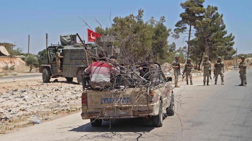 Syrians sit in the back of a passing pick-up truck loaded with wood as Turkish soldiers deploy at the site of an improvised explosive device which hit a joint Turkish-Russian patrol on the strategic M4 highway, near the Syrian town of Ariha in the rebel-held northwestern Idlib province, on July 14, 2020. - Three Russian and several Turkish soldiers were wounded in Syria's restive Idlib province when a joint military patrol was hit by an improvised explosive device, Russia's defence ministry said. (Photo by 