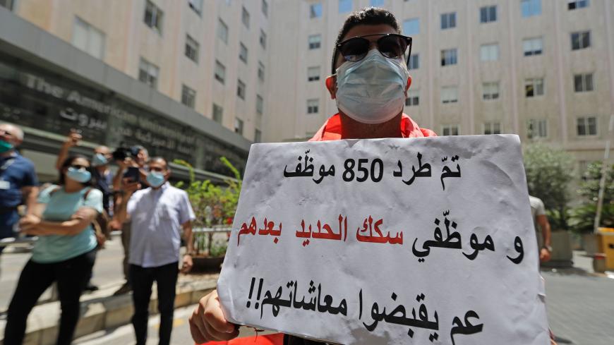 A Lebanese protester lifts a placard which reads "850 staff were laid-off while staff of the (defunct) railroads sector still get paid" during a demonstration of former employees of the American University Medical Center outside the hospital in the capital Beirut, on July 20, 2020, after they were dismissed from their jobs last week as part of a series of sweeping layoffs planned for the American University of Beirut and its medical center to cope with a severe recession resulting from the country's economi