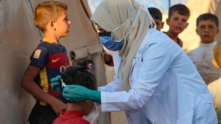 A Syrian doctor, on her own initiative, instructs children how to properly wear a mask during the novel coronavirus pandemic crisis, in the displacement camp of Janid near the town of Dana, east of the Turkish-Syrian border in the northwestern Idlib province, on July 26, 2020. (Photo by Ibrahim YASOUF / AFP) (Photo by IBRAHIM YASOUF/AFP via Getty Images)