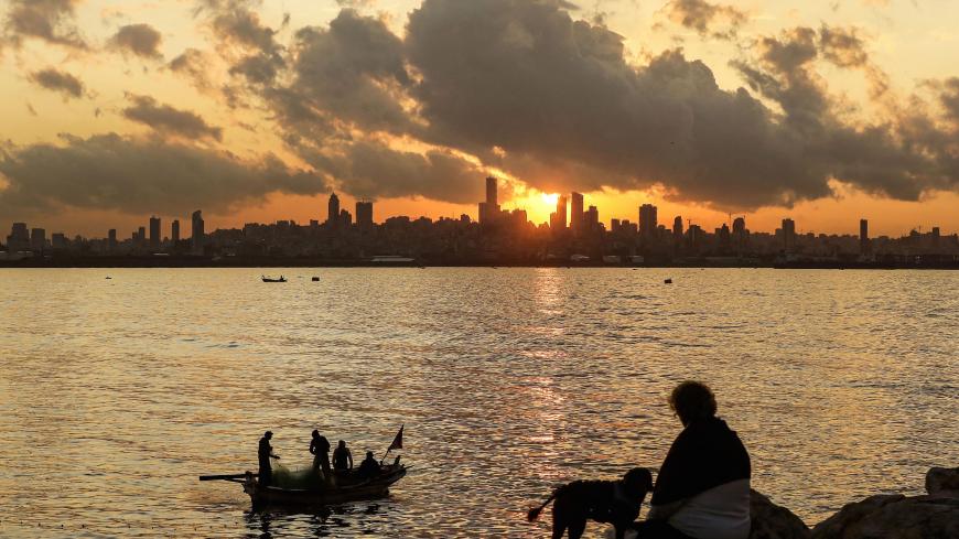 A woman sits with a dog over the Mediterranean sea waterfront by a fishing boat in the area of Dbayeh, north of the capital Beirut (background skyline), before sunset on December 5, 2019. (Photo by JOSEPH EID / AFP) (Photo by JOSEPH EID/AFP via Getty Images)