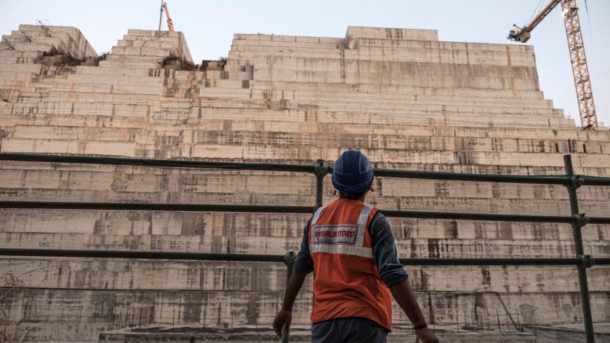 A construction worker looks at the Grand Ethiopian Renaissance Dam (GERD), near Guba in Ethiopia, on December 26, 2019. - The Grand Ethiopian Renaissance Dam, a 145-metre-high, 1.8-kilometre-long concrete colossus is set to become the largest hydropower plant in Africa.
Across Ethiopia, poor farmers and rich businessmen alike eagerly await the more than 6,000 megawatts of electricity officials say it will ultimately provide. 
Yet as thousands of workers toil day and night to finish the project, Ethiopian ne