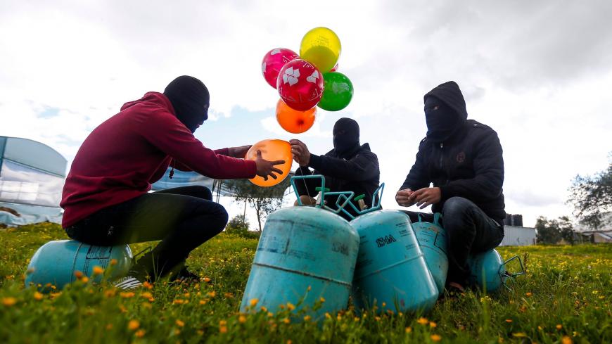 TOPSHOT - Masked Palestinians prepare to attach balloons to a gas canister before releasing it with an incendiary device near Gaza's Bureij refugee camp, along the Israel-Gaza border fence, on February 10, 2020. (Photo by MAHMUD HAMS / AFP) (Photo by MAHMUD HAMS/AFP via Getty Images)