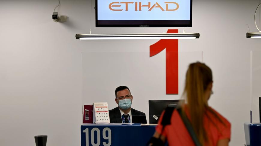 An airport personnel wearing a protective face mask, serves a passenger behind plexiglas at the Etihad check-in counter at Belgrade's airport on May 21, 2020, as Serbia's national carrier, Air Serbia, and United Arab Emirates' Etihad Airways resume commercial flights following the government's easing of lockdown measures against the spread of the novel coronavirus, COVID-19, pandemic. - With limited number of flights, air travel has resumed at Serbia's main airport after the authorities approved the airport