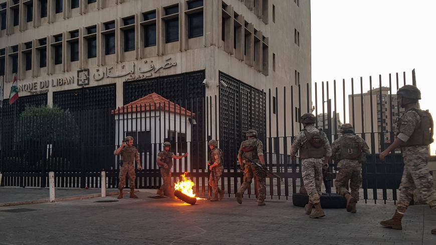 Lebanese Army soldiers roll away a flaming tire from the fence surrounding the local branch of the Banque du Liban (Lebanese Central Bank) as protesters gather to demonstrate against dire economic conditions in the northern city of Tripoli on June 11, 2020. - The Lebanese pound sank to a record low on the black market on June 11 despite the authorities' attempts to halt the plunge of the crisis-hit country's currency, money changers said. Lebanon is in the grips of its worst economic turmoil in decades, and