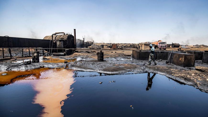 A man walks at a makeshift refinery using burners to distill crude oil in the village of Bishiriya in the countryside near the town of Qahtaniya west of Rumaylan (Rmeilan) in Syria's Kurdish-controlled northeastern Hasakeh province, on July 19, 2020. - Oil pollution in Syria has become a growing concern since the 2011 onset of a civil war that has taken a toll on oil infrastructure and seen rival powers compete over control of key hydrocarbon fields. In the Kurdish-held northeast, a large storage facility i