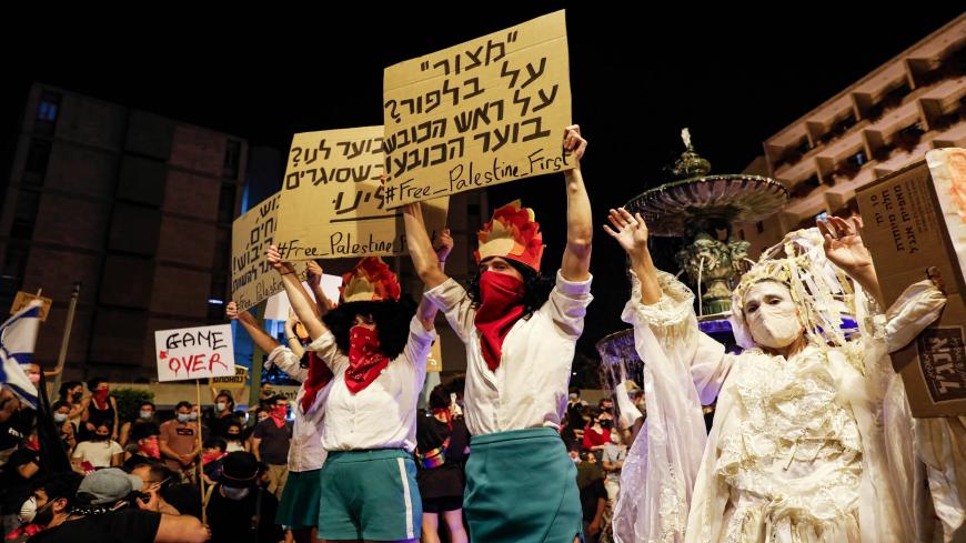A protester wearing a bandana around the mouth stands with others holding up a sign (R) reading in Hebrew "'siege' on Balfour"" (referencing the street near the Israeli Prime Minister's residence) and "on the head of the thief the hat burns" (proverb), during a demonstration against the Israeli government near the Prime Minister's residence in Jerusalem on July 25, 2020. (Photo by Ahmad GHARABLI / AFP) (Photo by AHMAD GHARABLI/AFP via Getty Images)