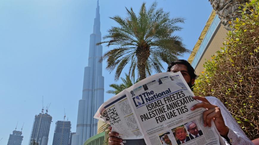 A man reads a copy of UAE-based The National newspaper near the Burj Khalifa, the tallest structure and building in the world since 2009, in the gulf emirate of Dubai on August 14, 2020, as the publication's headline reflects the previous day's news as Israel and the UAE agreed to normalise relations in a landmark US-brokered deal. - The deal marks only the third such accord the Jewish state has struck with an Arab nation, an historic shift making the Gulf state only the third Arab country to establish full