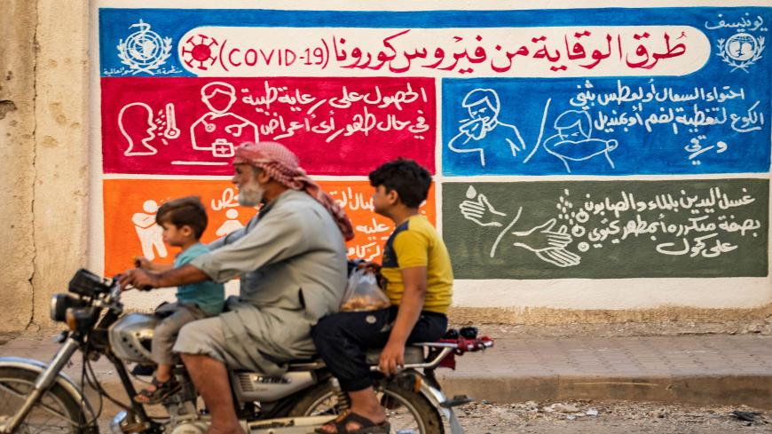 Syrians ride a motorbike past a mural painted as part of an awareness campaign by the United Nations International Children's Emergency Fund (UNICEF) and World Health Organization (WHO) intitative, bearing instructions on protection from COVID-19 in the Kurdish-majority city of Qamishli of Syria's northeastern Hasakeh province on August 16, 2020, after a spike in infections in the area. (Photo by Delil SOULEIMAN / AFP) (Photo by DELIL SOULEIMAN/AFP via Getty Images)