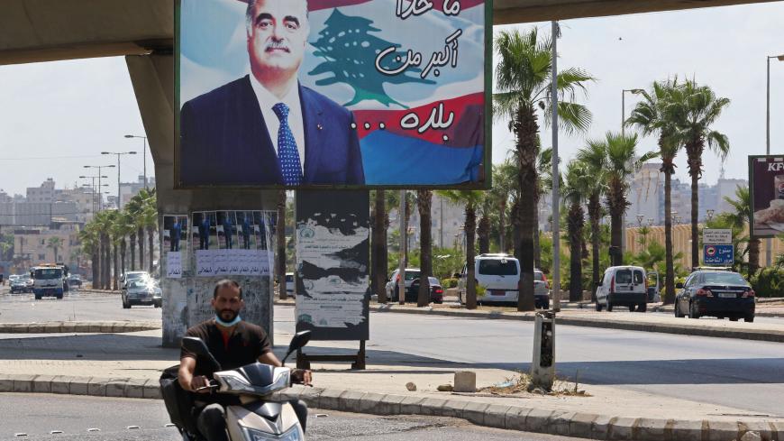 A man rides a motorbike past a billboard bearing a picture of slain Lebanese Prime Minister Rafiq Hariri, on a street in his southern hometown city of Sidon (Saida), on August 18, 2020. - On February 14, 2005, the former Premier, who embodied the reconstruction of the country after its 1975-1990 civil war was killed in a monster bomb attack on his convoy. The special tribunal trying the four suspects accused of the assassination is expected to deliver its verdict today. (Photo by Mahmoud ZAYYAT / AFP) (Phot
