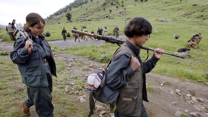Kurdish Peshmerga militiamen carry their weapons as other fighters play volleyball at one of their camps in the Qandil Mountains located along the Iraq-Iran border, 05 May 2006. A top Kurdish guerilla threatened 06 May to launch hit-and-run attacks on Iran, saying the Shiite country planned to bomb his group's positions inside Iraq to gain Turkey's support against the US.  AFP PHOTO/ALI AL-SAADI        (Photo credit should read ALI AL-SAADI/AFP via Getty Images)