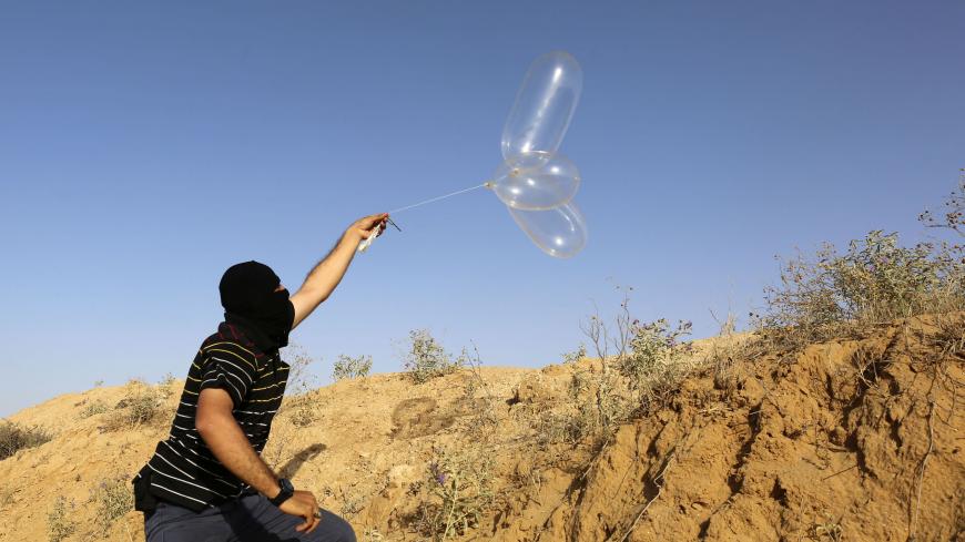 A masked Palestinian launches a Balloon loaded with flammable materials to be flown toward Israel, at the Israel-Gaza border, in Rafah in the southern Gaza Strip on June 17, 2018. (Photo by SAID KHATIB / AFP)        (Photo credit should read SAID KHATIB/AFP via Getty Images)