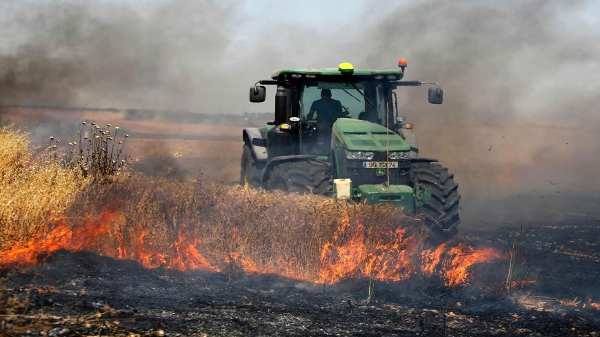 An Israeli farmer uses a tractor in an attempt to extinguish a fire in a wheat field near the Kibbutz Nahal Oz, along the border with the Gaza Strip, on May 15, 2019 after it was caused by inflammable material attached to helium balloon flown by Palestinian protesters from across the border. - Palestinians are marking the 1948 Nakba, or "catastrophe", which left hundreds of thousands of Palestinians displaced by the war accompanying the birth of the Jewish state. (Photo by Menahem KAHANA / AFP)        (Phot
